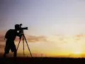 Sylwetka fotografa z aparatem na statywie na tle zachodzącego słońca i farmy wiatrowej. Zastanawiam się, ile bierze fotograf za 18 takich ujęć.