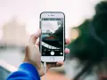 Dłoń trzyma smartfon, na ekranie którego widać interfejs aparatu i miejski krajobraz. Robię zdjęcia z telefonu.