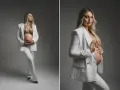 Elegancka kobieta w białym garniturze podczas sesji ciążowej, czule trzymająca się za brzuch.